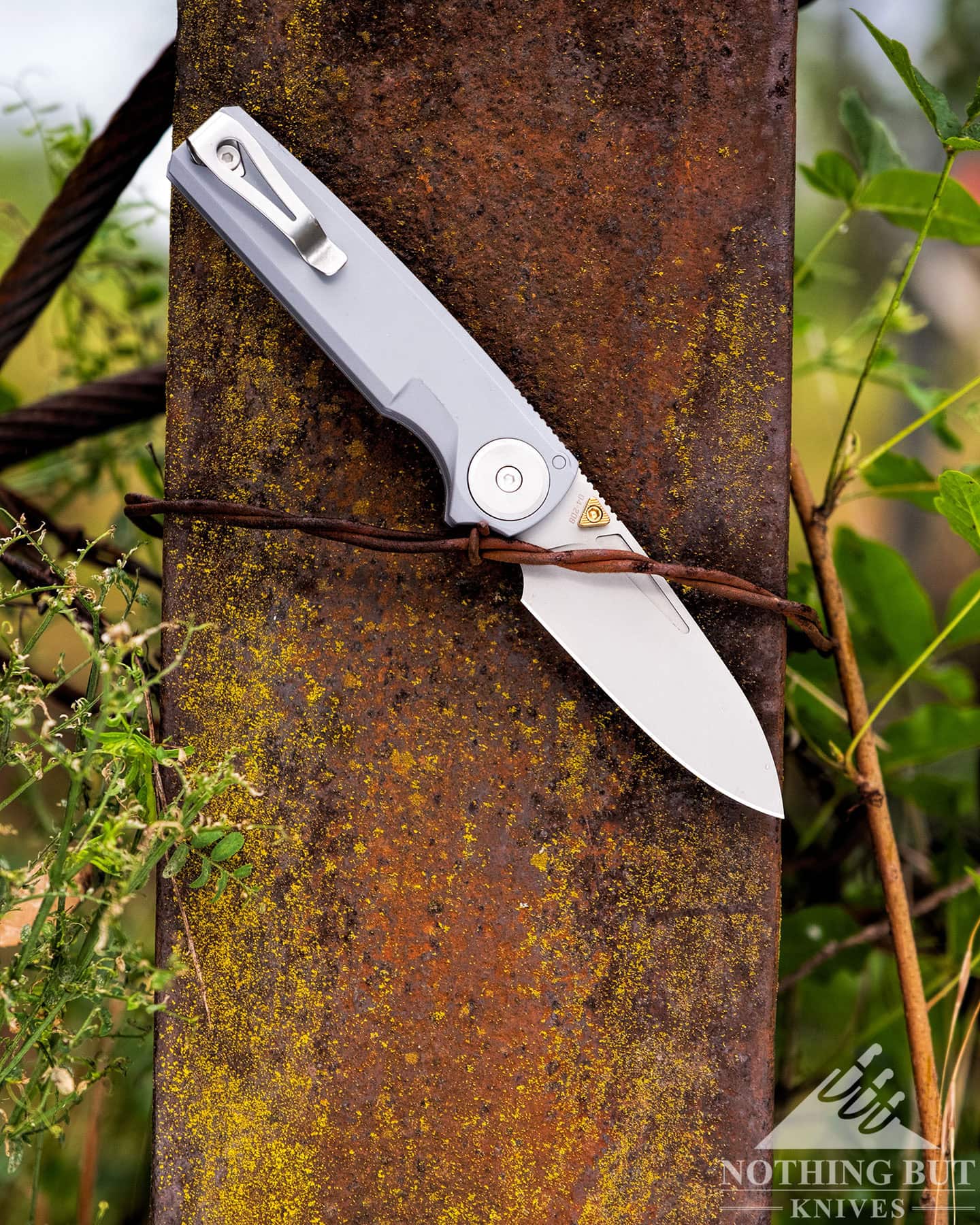 Worksharp Rmx Thumbstud Knife Review - Image 12 A profile image showing the Work Sharp RMX pocket knife with its blade in the open position wedged behind a strand of barbed wire on a rusty steel I-beam.