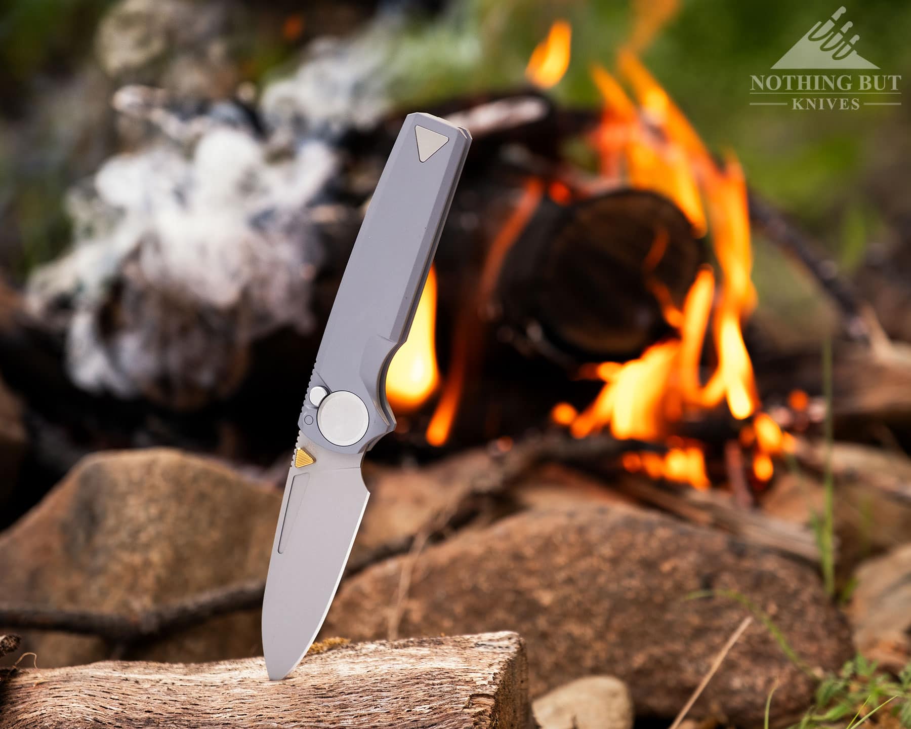 Worksharp Rmx Thumbstud Knife Review - Image 3 The Work Sharp RMX knife sticking out of a piece of firwood in front of a campfire in the forest.