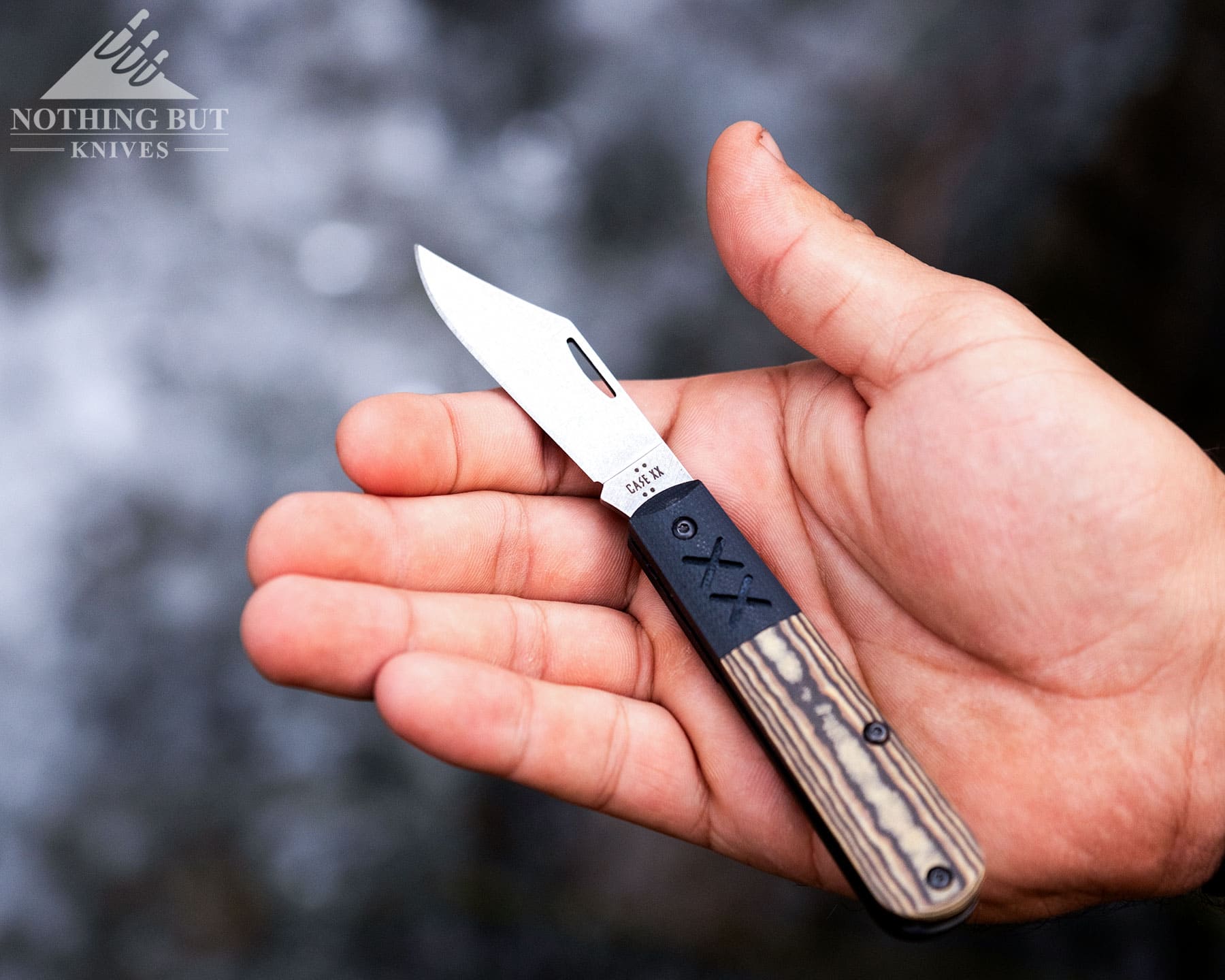 An overhead view of the Case Crossroads folding knife shown with the blade fully open in the palm of a person's open hand above a creek,