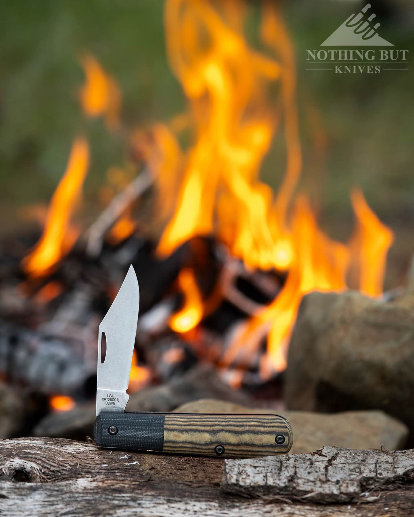 The Case Crossroads Barlow knife in the half open position on a piece of firewood next to a campfire. 