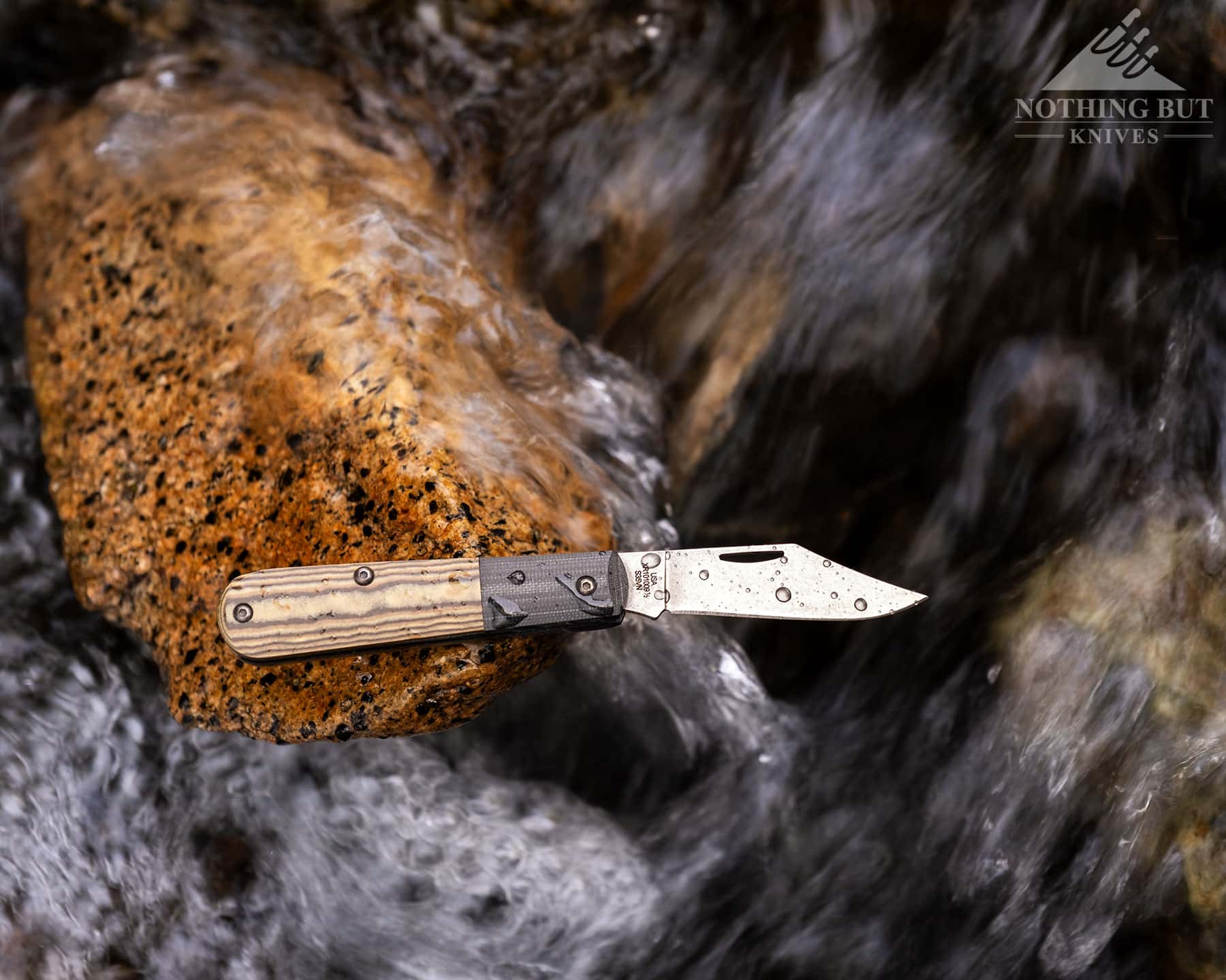An overhead view of the Case Crossroads Barlow with its blade open balanced on a rock next to a creek. 