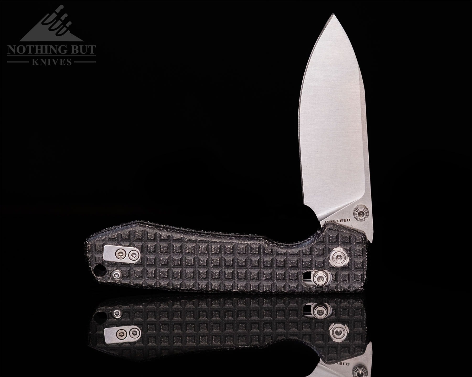 Worksharp Rmx Thumbstud Knife Review - Image 11 The Vosteed Racoon folder shown here with its blade in the half open position on a reflective surface in front of a black background.
