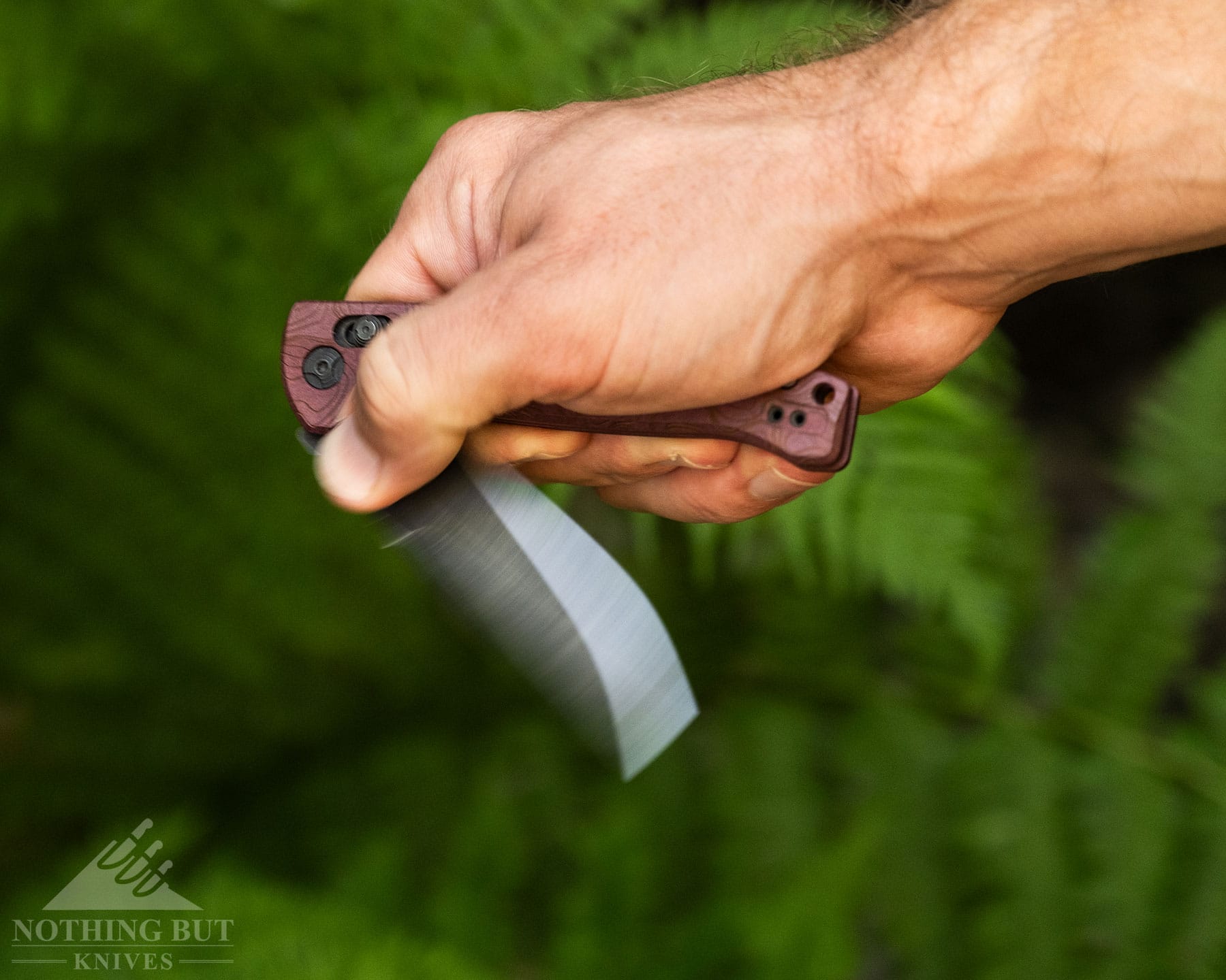 Hogue Mysto Review - Image 6 A slightly elevated angle view of the Hogue Mysto folding knife being flipped open in front of green fern plants.