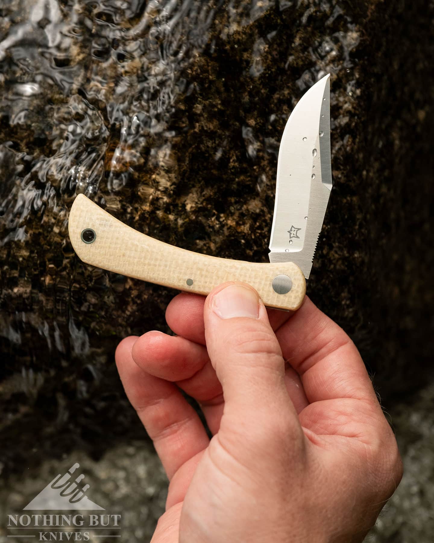 An overhead view of the Fox Knives Mi Libar slip joint knife being held above a creek in a person's right hand.